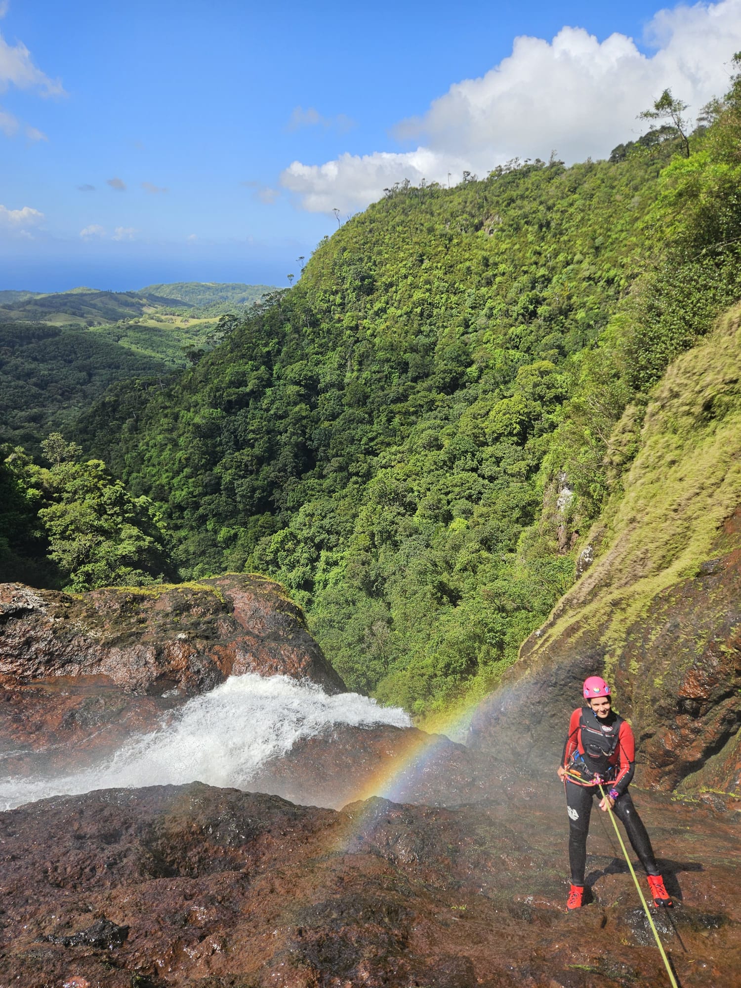 Abseilen am Wasserfall mit weitem Blick über die grüne Landschaft.